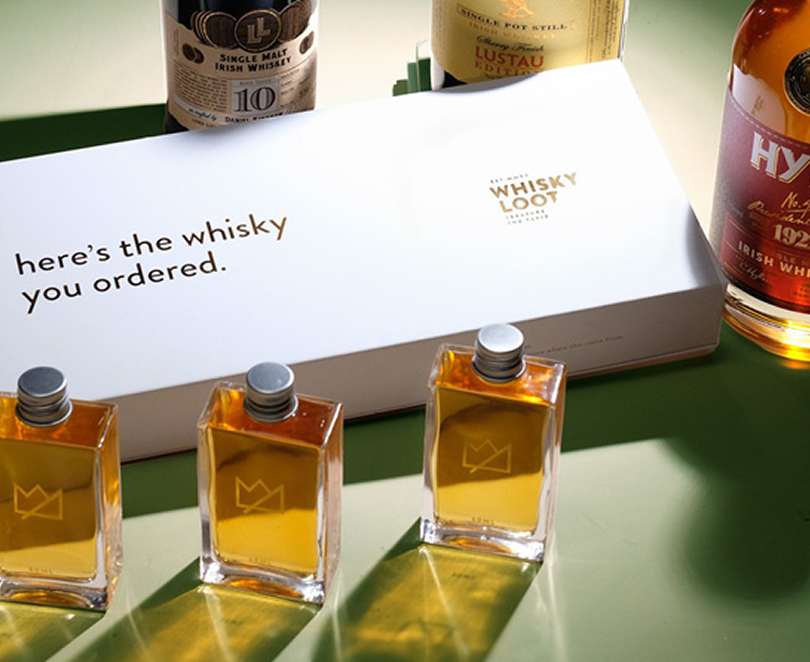 A set of liquor bottles on a table with a glass of whiskey behind them.